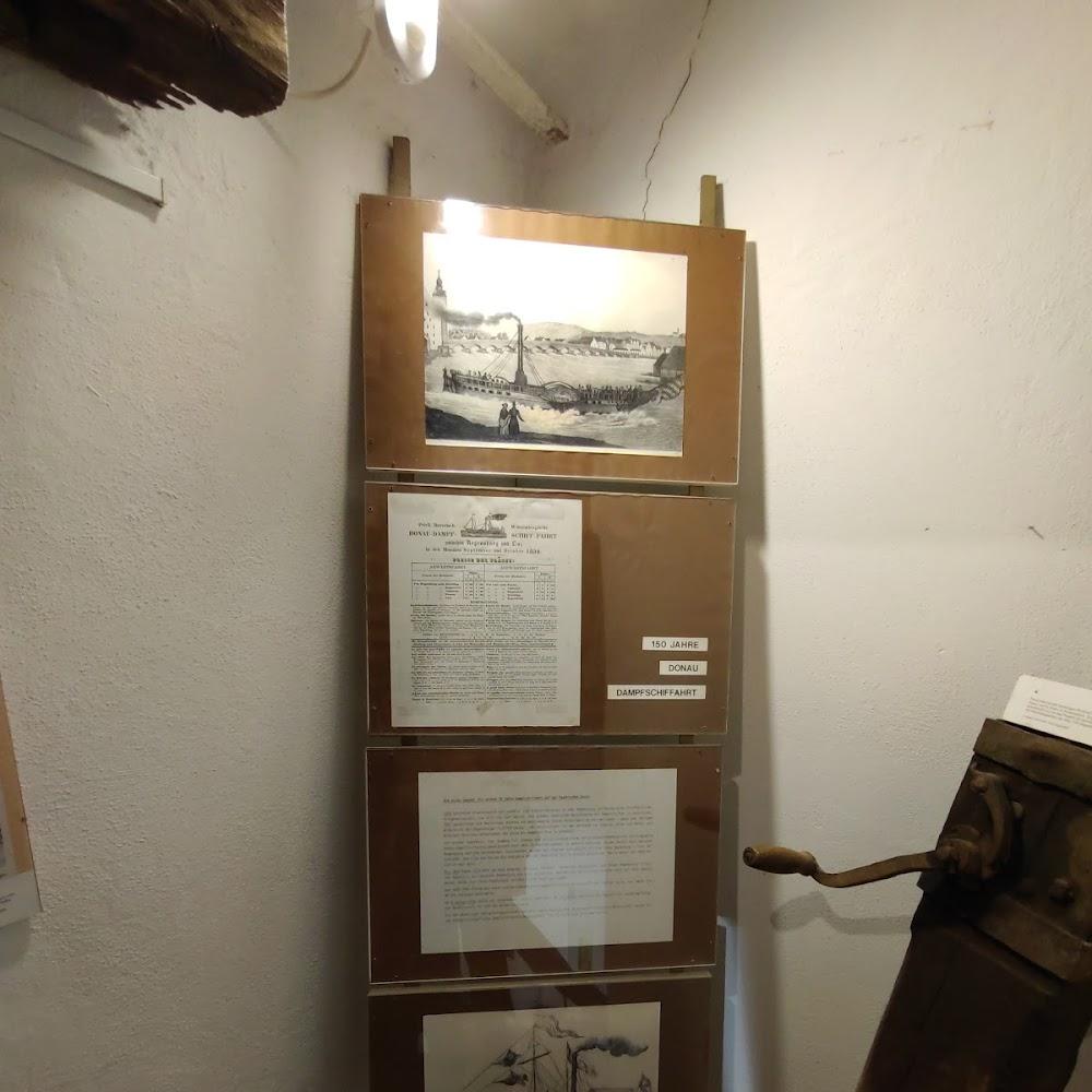 Four framed documents and a wooden machine. 
150 Jahre Donauschiffahrt.